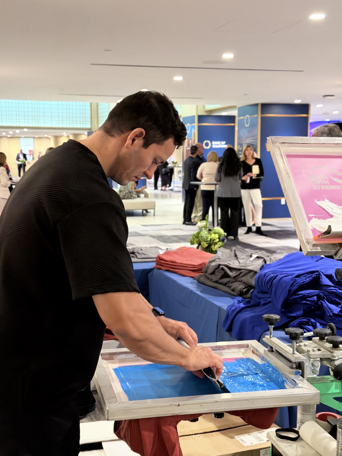Person performing a screen printing demonstration with vibrant blue ink on merchandise at a trade show